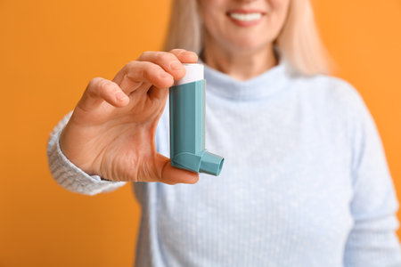 Mature woman with inhaler on color background