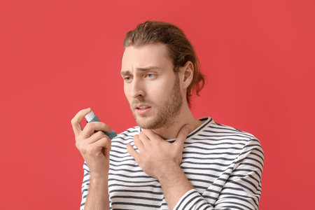 Young man with inhaler having asthma attack on color backgroundの写真素材