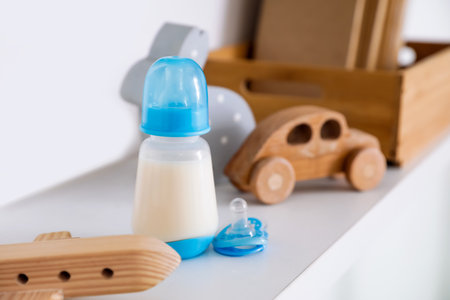 Bottle of milk for baby with toys on shelf, closeupの写真素材