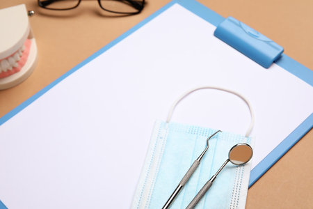 Clipboard with medical mask and dental tools on brown background, closeupの写真素材