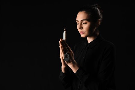 Young woman with candle and military tag praying on black background.の写真素材