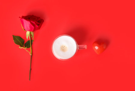 Glass cup of latte, heart and rose on red background. Valentine's Day celebrationの写真素材
