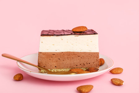 Plate with piece of birds milk cake, almond nuts and spoon on pink backgroundの写真素材