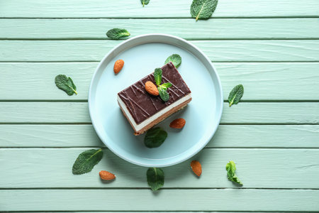 Plate with piece of birds milk cake, almond nuts and mint leaves on wooden backgroundの写真素材