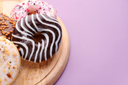 Wooden board with delicious donuts on lilac background, closeupの写真素材