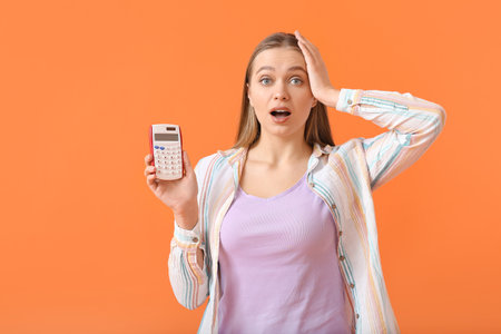 Surprised woman with calculator on color backgroundの写真素材