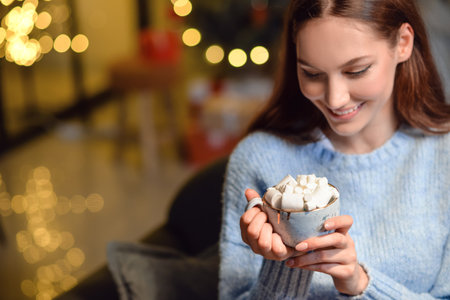Beautiful young woman with cup of hot cacao drink at home on Christmas eveの写真素材