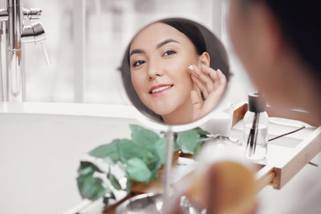 Beautiful Asian woman applying cream in bathroomの写真素材