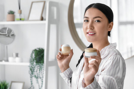 Beautiful Asian woman with jars of cream in bathroomの写真素材