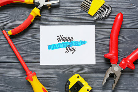 Composition for Father's Day with greeting card and tools on wooden background