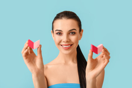 Beautiful young woman with makeup sponges on color backgroundの写真素材