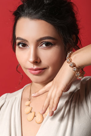 Beautiful young woman wearing stylish jewelry on color background