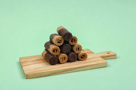 Board with chocolate wafer rolls on green backgroundの写真素材
