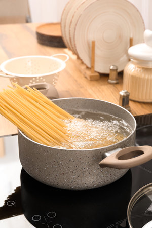 Cooking pot with raw pasta and boiling water on electric stove in kitchenの写真素材