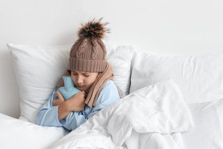 Ill girl with hot water bottle lying in bed at homeの写真素材