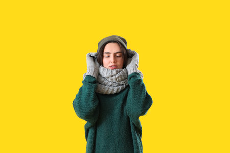 Frozen young woman in winter clothes on yellow backgroundの写真素材
