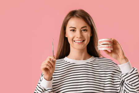 Young woman with dental tool and jaw model on pink background