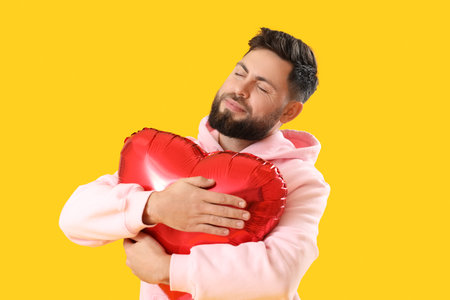 Young bearded man with balloon for Valentine's Day on yellow backgroundの写真素材