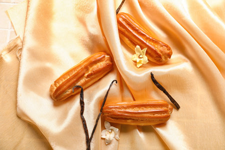 Sweet eclairs and vanilla sticks on fabric background