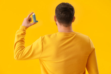 Man with inhaler on yellow background, back viewの写真素材