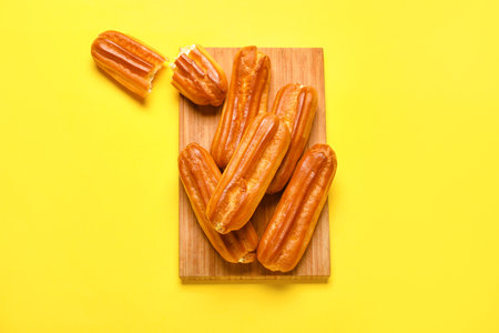 Wooden board with sweet eclairs on yellow background