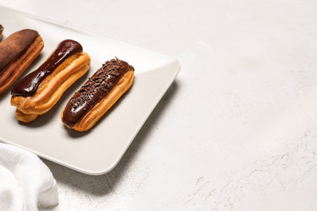 Plate of sweet chocolate eclairs on light background