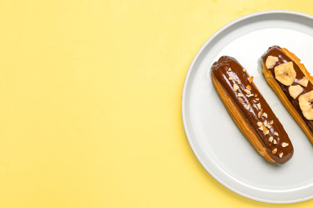Plate with tasty chocolate eclairs on yellow backgroundの写真素材