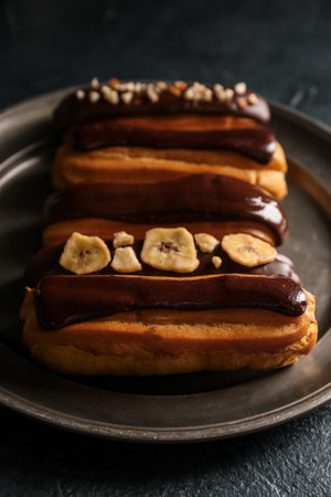 Plate of sweet chocolate eclairs on dark color background, closeup