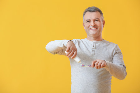 Mature man brushing teeth on color backgroundの写真素材