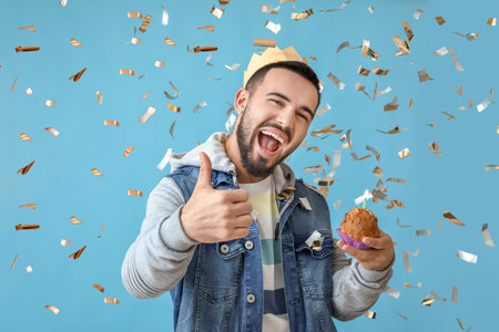 Young man with birthday cupcake showing thumb-up on color backgroundの写真素材
