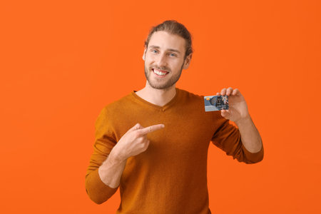 Handsome young man with gift card on color backgroundの写真素材