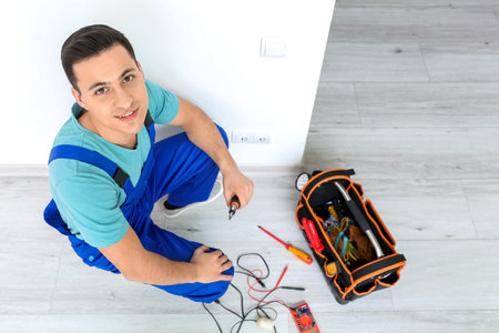 Young electrician repairing socket in room