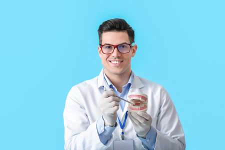 Male dentist with plastic jaw model on color background