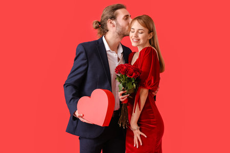 Young couple with flowers and gift on color background. Valentine's Day celebrationの写真素材