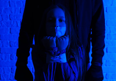 Terrorist and scared little hostage on brick backgroundの写真素材