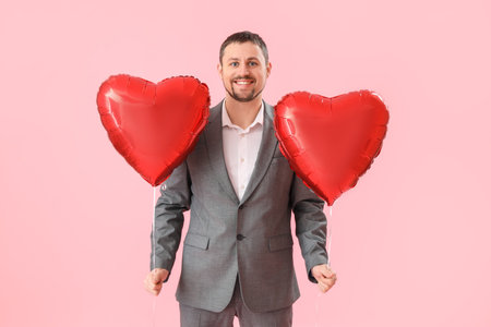 Handsome man with heart-shaped balloons on pink background. Valentine's Day celebrationの写真素材