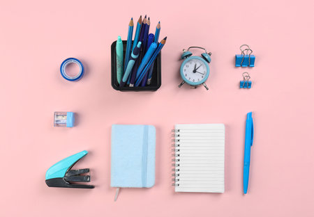 Holder with stationery, notebooks and alarm clock on pink backgroundの写真素材