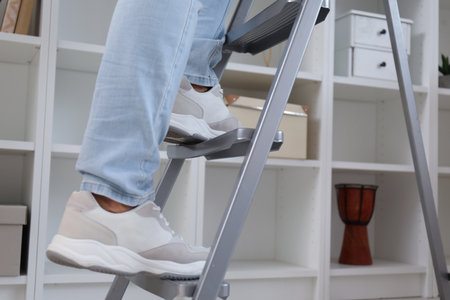Young man on ladder near bookshelf at home, closeupの写真素材