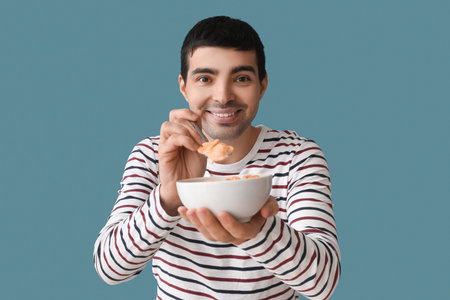 Young man eating cornflakes with spoon on color background, closeupの写真素材