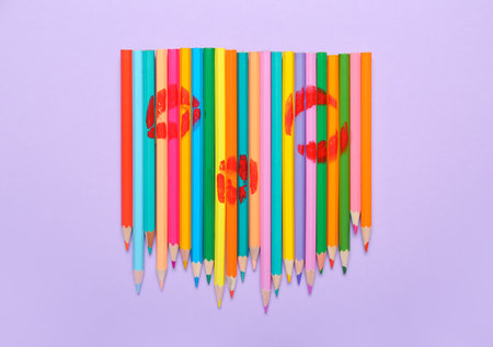 Colorful pencils with lipstick kiss marks on lilac background