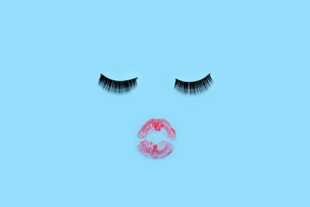Face made of fake eyelashes and lipstick kiss mark on blue backgroundの写真素材