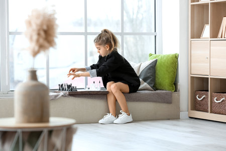 Cute little girl playing chess at homeの写真素材