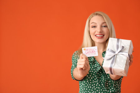 Beautiful young woman with gift card and present on color background