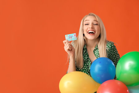 Beautiful young woman with gift card and balloons on color backgroundの写真素材