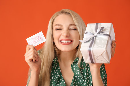 Beautiful young woman with gift card and present on color backgroundの写真素材