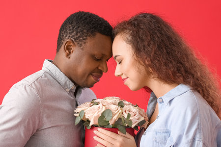 African-American couple with flowers on color background. Valentine's Day celebrationの写真素材