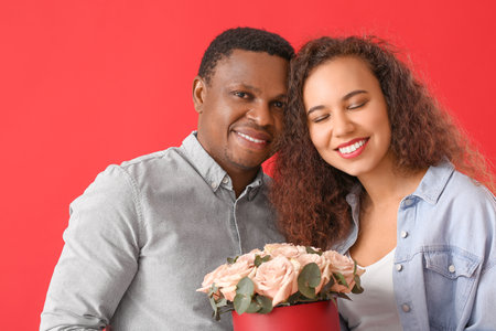 African-American couple with flowers on color background. Valentine's Day celebrationの写真素材