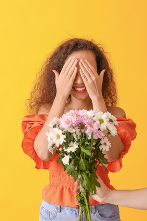African-American woman receiving bouquet of beautiful flowers on color backgroundの写真素材