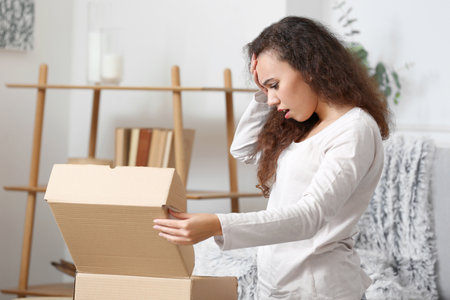 Upset young woman unpacking parcel at home