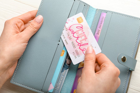 Woman putting gift card in wallet on white wooden background, closeup